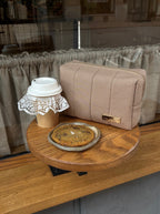 Small round wooden table with a cookie, coffee cup, and beige makeup bag in a casual setting.