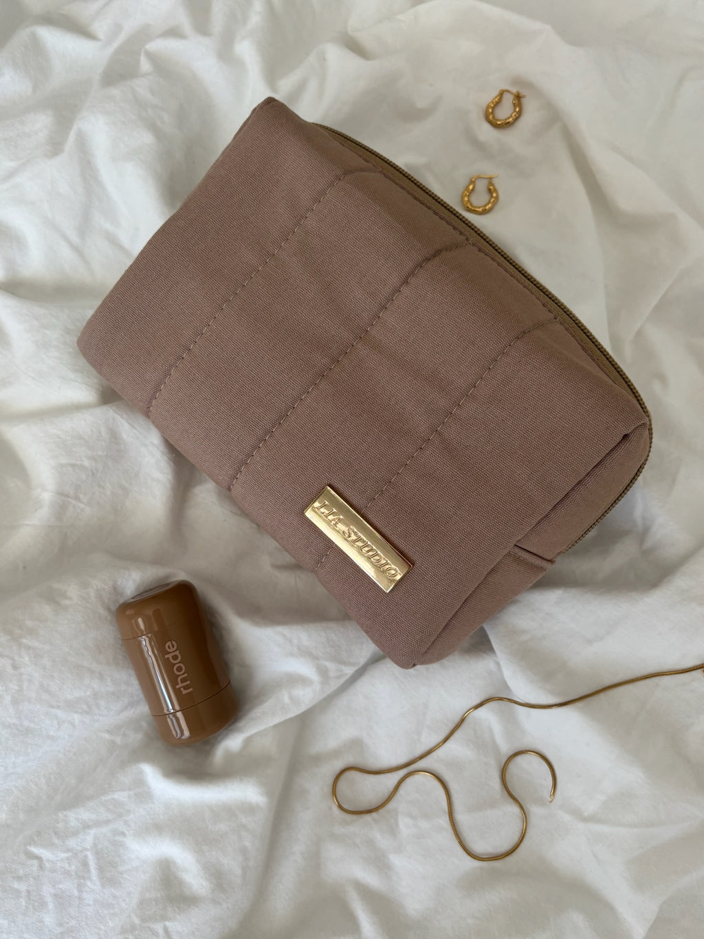 Beige  makeup bag with gold logo on a white textured surface