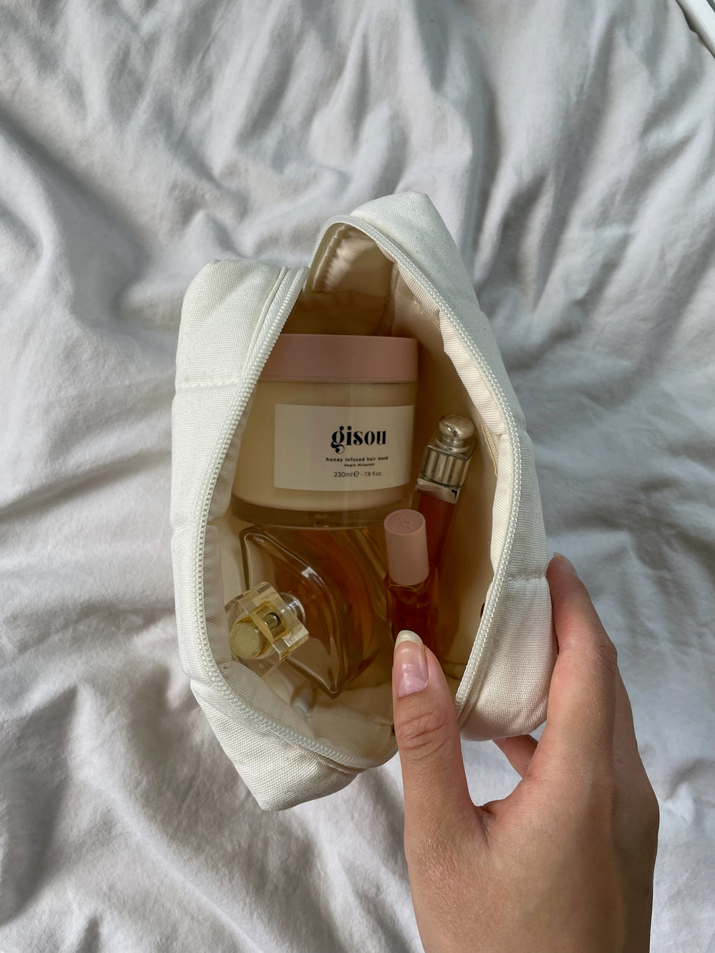 Hand holding open makeup bag with products inside