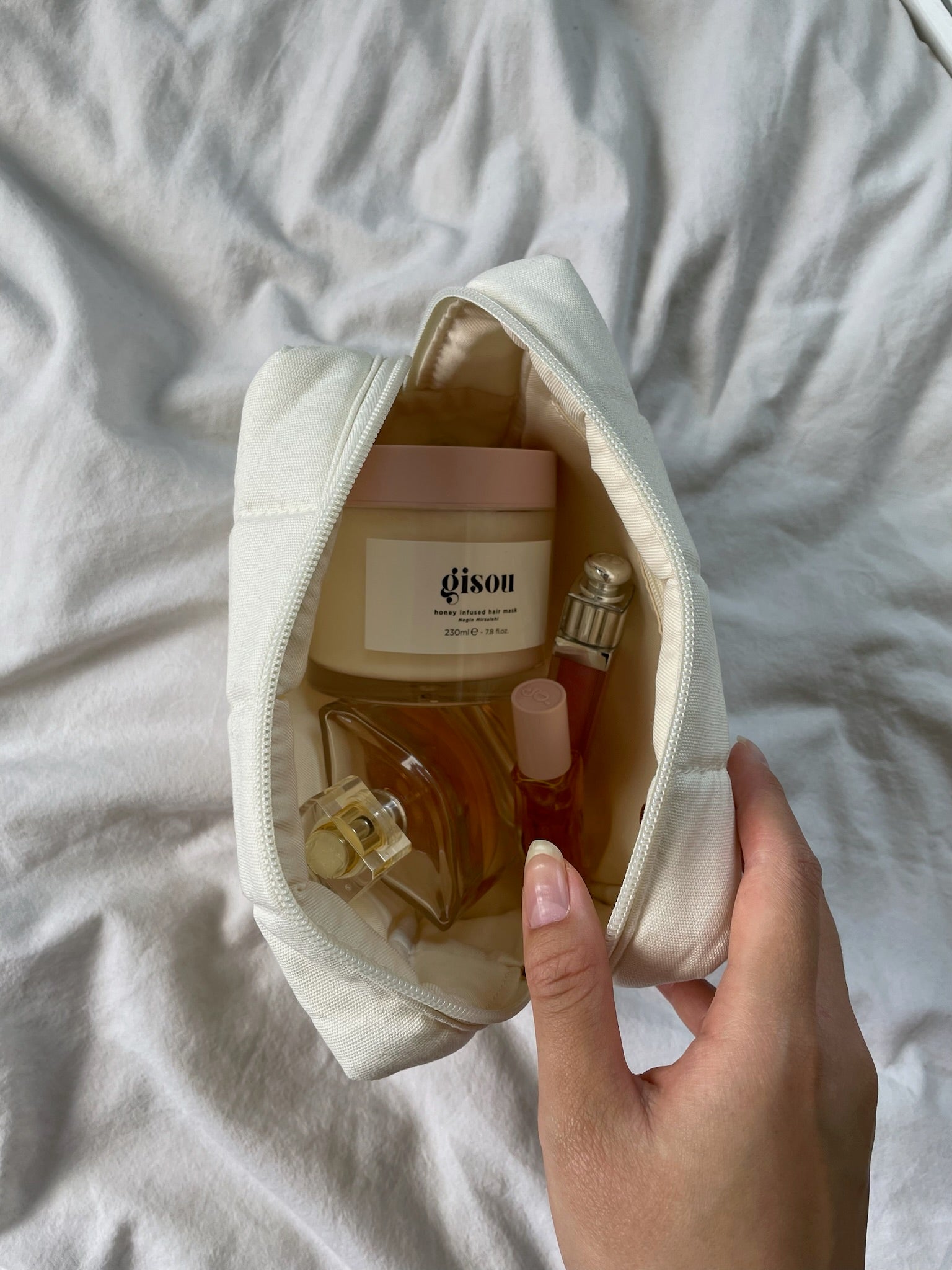 Hand holding open makeup bag with products inside