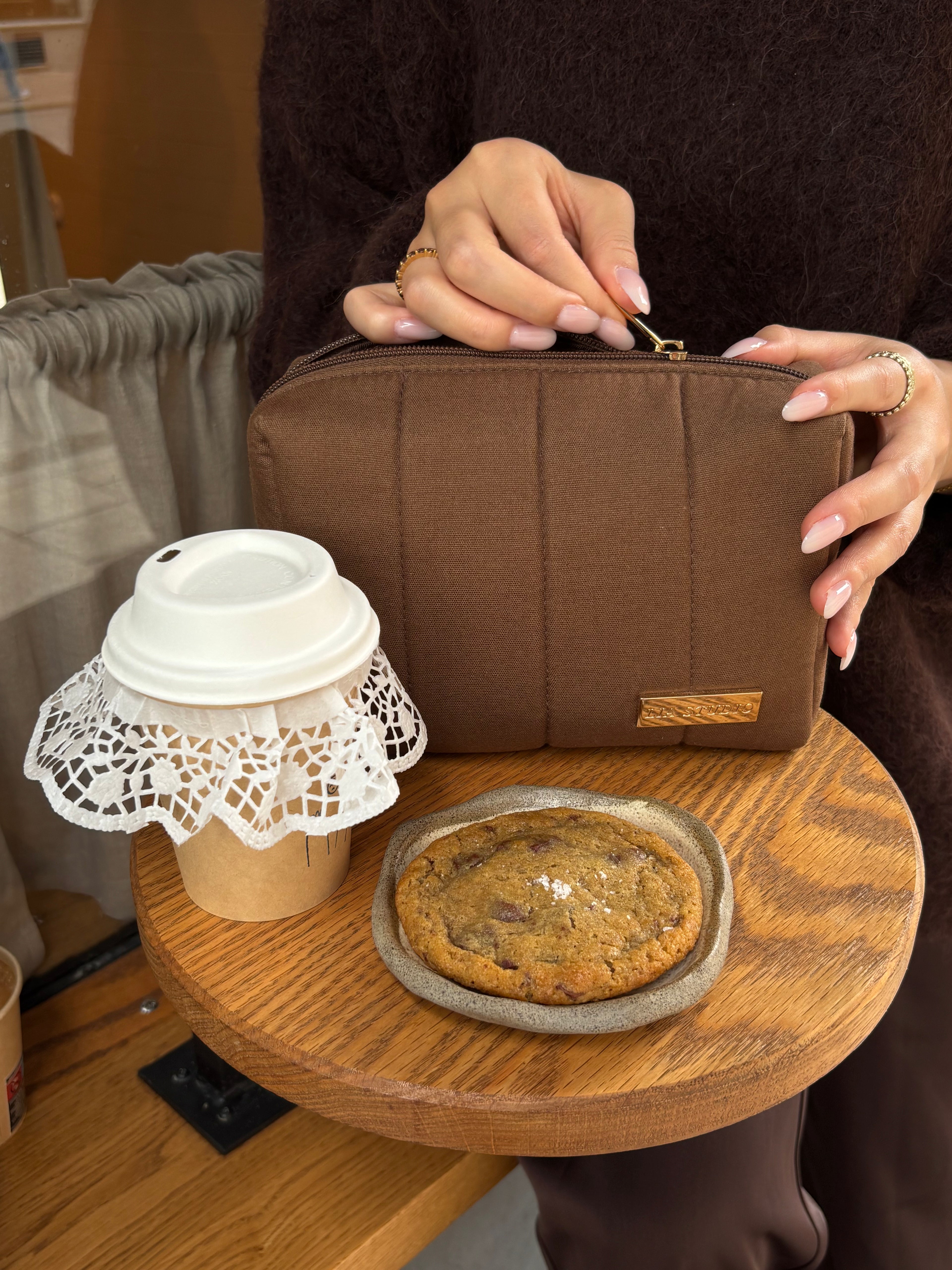 Person holding a brown pouch with a cookie and coffee cup on a wooden table.