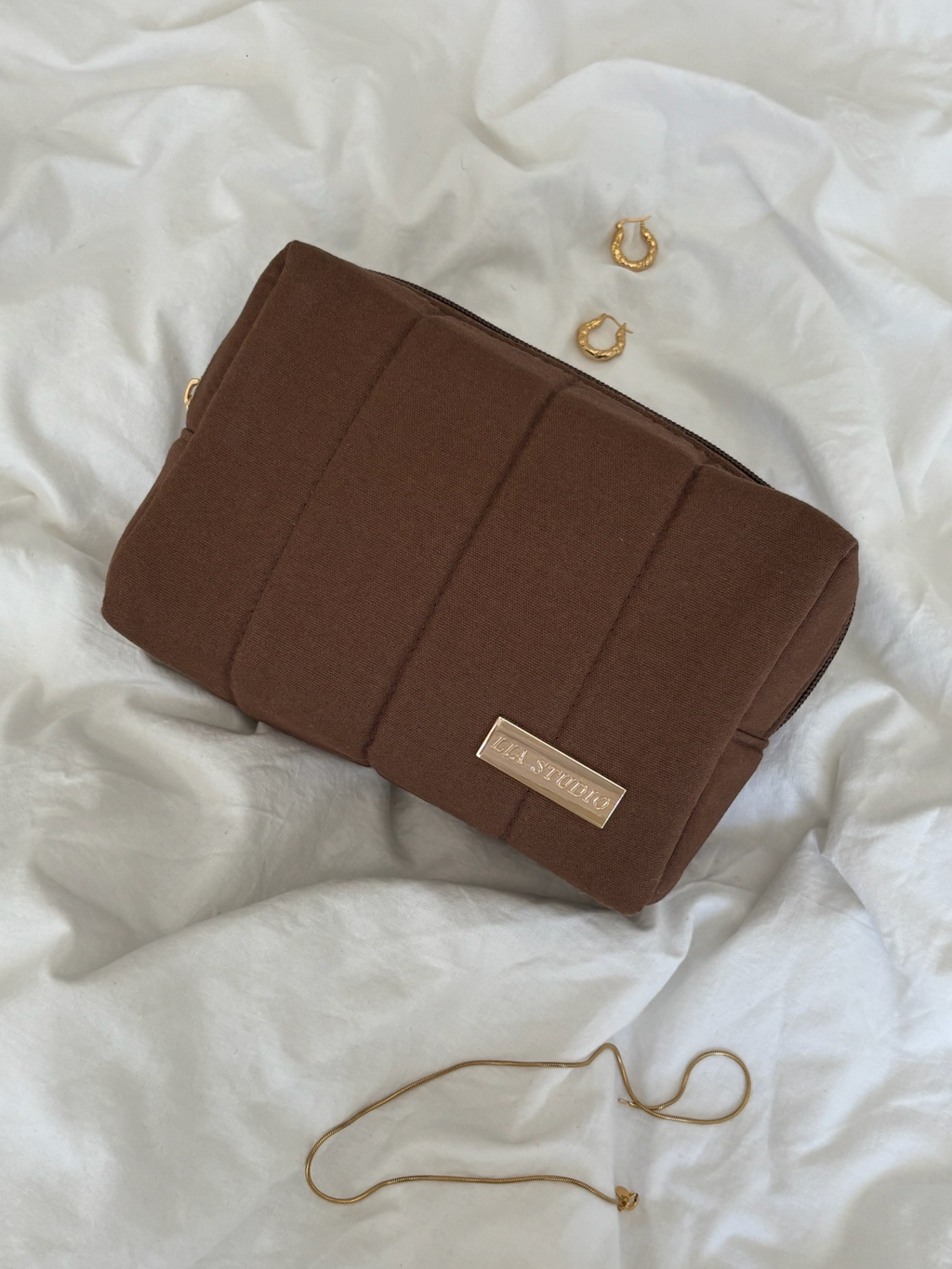 Brown makeup bag with a visible brand logo on a white textured surface