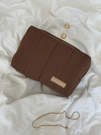 Brown makeup bag with a visible brand logo on a white textured surface