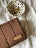 brown makeup bag tonka on white textured fabric by bowl with gold jewelry